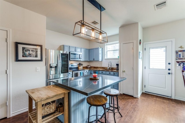 18701 Golden Eagle Way, Elgin, TX 78621 - kitchen featuring stainless steel appliances, dark countertops, a kitchen breakfast bar, blue cabinets, and dark wood-style flooring