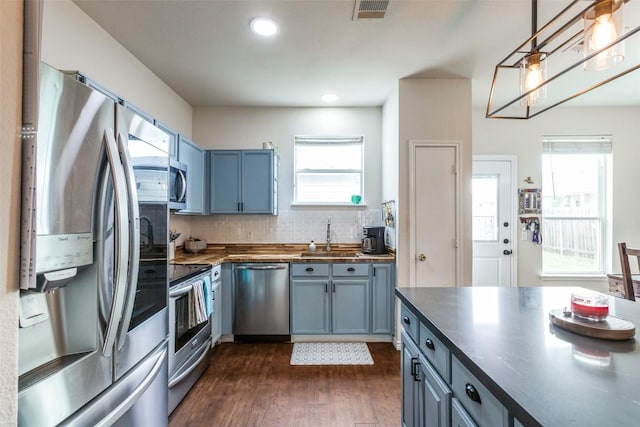 18701 Golden Eagle Way, Elgin, TX 78621 - kitchen with appliances with stainless steel finishes, dark wood-type flooring, decorative backsplash, blue cabinetry, and decorative light fixtures