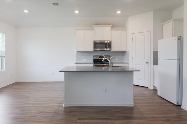 421 Bluejack Way, Hutto, TX 78634 - kitchen featuring stainless steel appliances, decorative backsplash, dark wood-style floors, dark countertops, and a kitchen island with sink