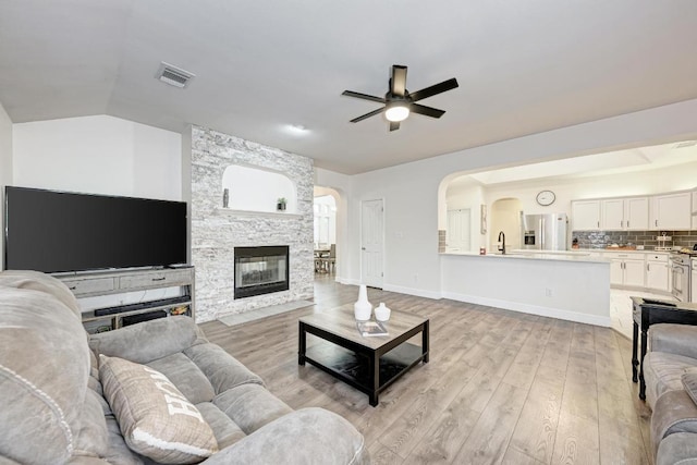 500 Olympic Dr, Pflugerville, TX 78660 - living room featuring ceiling fan, light wood-style floors, arched walkways, a stone fireplace, and vaulted ceiling