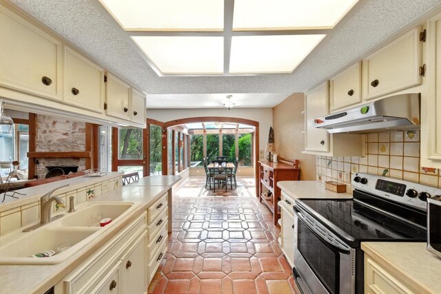 2500 Dana Cv, Austin, TX 78746 - kitchen with stainless steel electric range, under cabinet range hood, cream cabinets, decorative backsplash, and light countertops