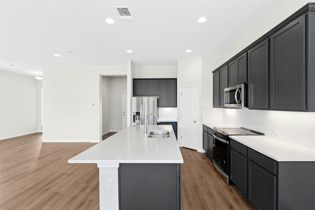 320 Creek Rd Unit 302, Dripping Springs, TX 78620 - kitchen featuring appliances with stainless steel finishes, light wood-type flooring, a center island with sink, tasteful backsplash, and recessed lighting