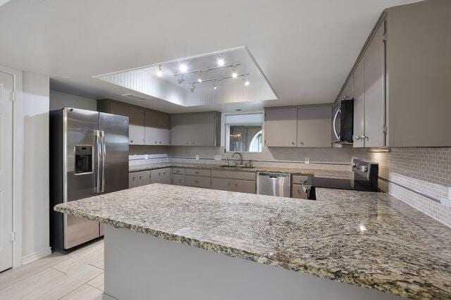 6203 Olympic Overlook Dr, Austin, TX 78746 - kitchen with appliances with stainless steel finishes, a raised ceiling, gray cabinets, backsplash, and a peninsula