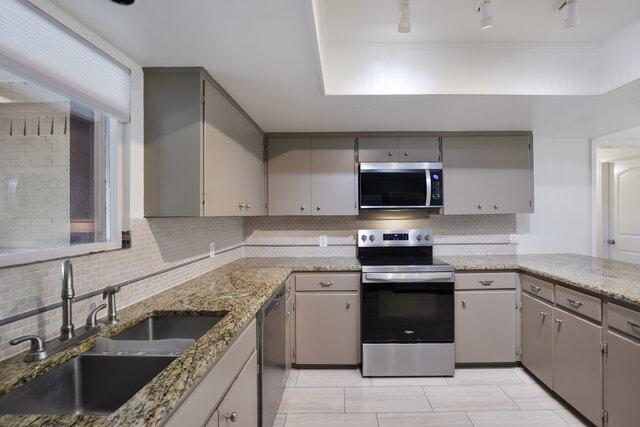 6203 Olympic Overlook Dr, Austin, TX 78746 - kitchen with appliances with stainless steel finishes, gray cabinets, decorative backsplash, light stone counters, and light tile patterned floors
