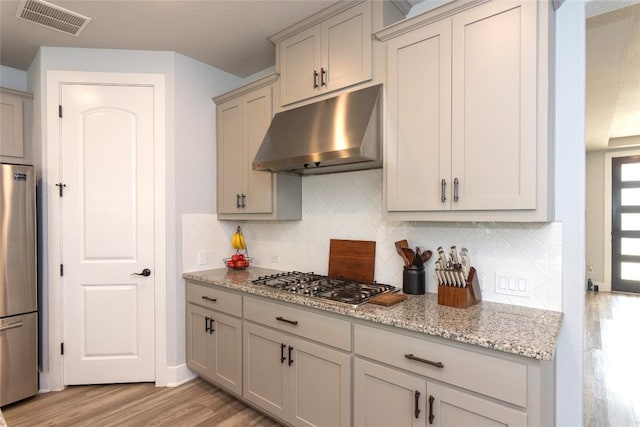 1328 Siena Sunset Rd, Leander, TX 78641 - kitchen featuring under cabinet range hood, stainless steel appliances, light wood-type flooring, tasteful backsplash, and light stone countertops