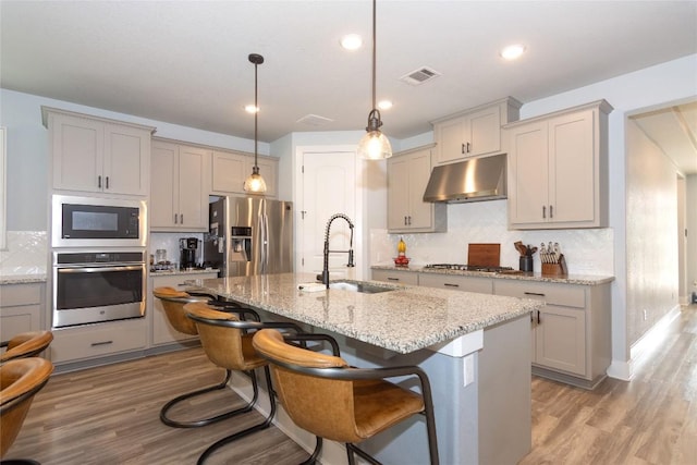 1328 Siena Sunset Rd, Leander, TX 78641 - kitchen with appliances with stainless steel finishes, under cabinet range hood, gray cabinetry, tasteful backsplash, and light stone counters