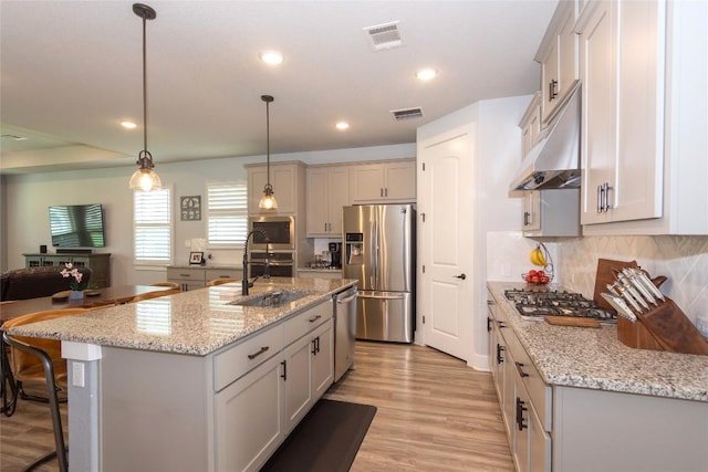 1328 Siena Sunset Rd, Leander, TX 78641 - kitchen featuring appliances with stainless steel finishes, under cabinet range hood, decorative backsplash, light wood-style floors, and a kitchen breakfast bar