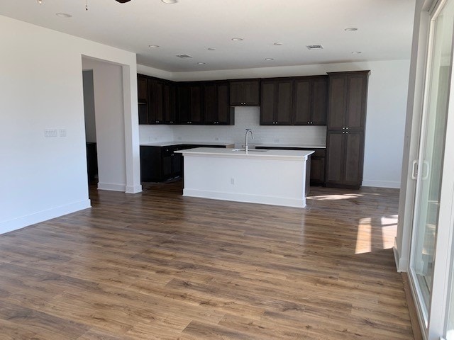 1104 Yaupon Holly Dr, Georgetown, TX 78628 - kitchen featuring a kitchen island with sink, wood finished floors, open floor plan, decorative backsplash, and dark brown cabinets