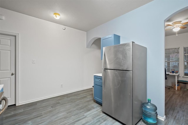 9206 Brents Elm Dr, Austin, TX 78744 - kitchen featuring freestanding refrigerator, blue cabinets, arched walkways, light wood-style floors, and a ceiling fan