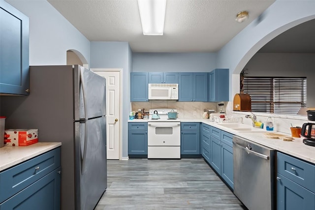 9206 Brents Elm Dr, Austin, TX 78744 - kitchen with appliances with stainless steel finishes, blue cabinets, light wood-style flooring, arched walkways, and light countertops