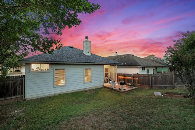 9206 Brents Elm Dr, Austin, TX 78744 - back of house at dusk with a fenced backyard, a deck, a chimney, and roof with shingles