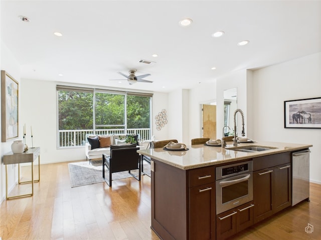 1600 Barton Springs Rd Unit 5107, Austin, TX 78704 - kitchen with stainless steel appliances, light stone countertops, light wood finished floors, dark brown cabinets, and a center island with sink