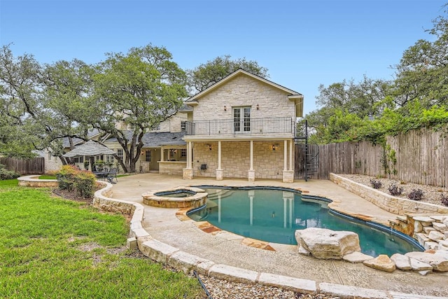 7503 Stonecliff Cir, Austin, TX 78731 - back of house featuring stone siding, a patio area, a balcony, a fenced backyard, and a pool with connected hot tub