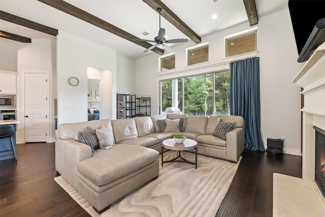 147 William Hersee Dr, Bastrop, TX 78602 - living room with a ceiling fan, a warm lit fireplace, dark wood-type flooring, beamed ceiling, and a towering ceiling