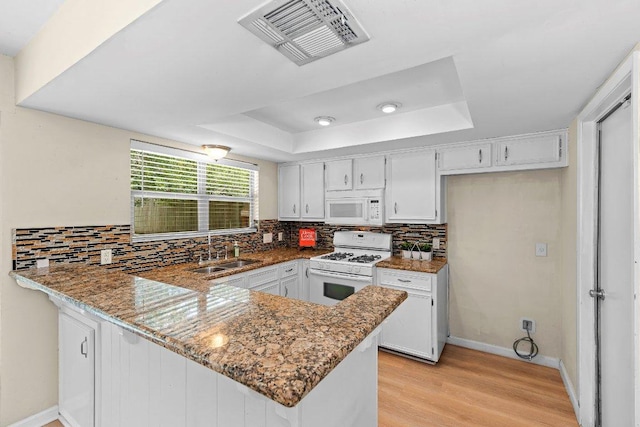 907 Great Oaks Cv, Round Rock, TX 78681 - kitchen with white appliances, a tray ceiling, a peninsula, backsplash, and light wood-style floors