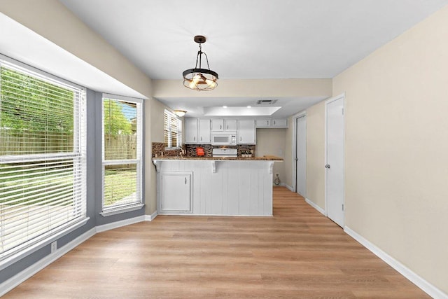 907 Great Oaks Cv, Round Rock, TX 78681 - kitchen featuring white microwave, a peninsula, light wood-type flooring, decorative light fixtures, and decorative backsplash