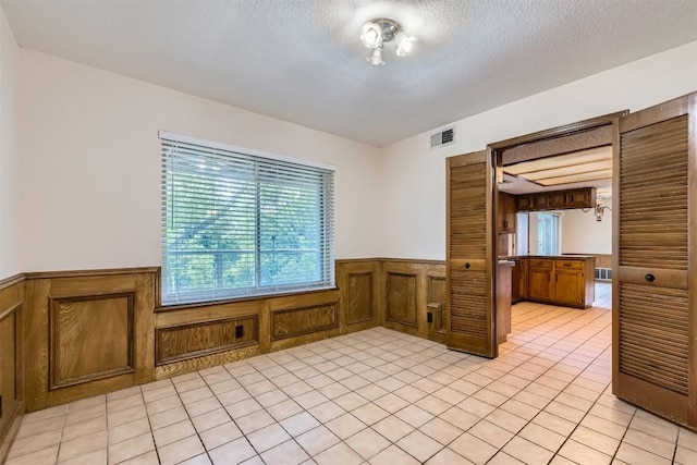 6819 Bayridge Ter, Austin, TX 78759 - unfurnished room with a wainscoted wall, light tile patterned floors, a textured ceiling, and wooden walls