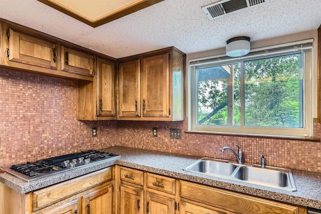 6819 Bayridge Ter, Austin, TX 78759 - kitchen featuring stainless steel gas cooktop, backsplash, a textured ceiling, and brown cabinetry