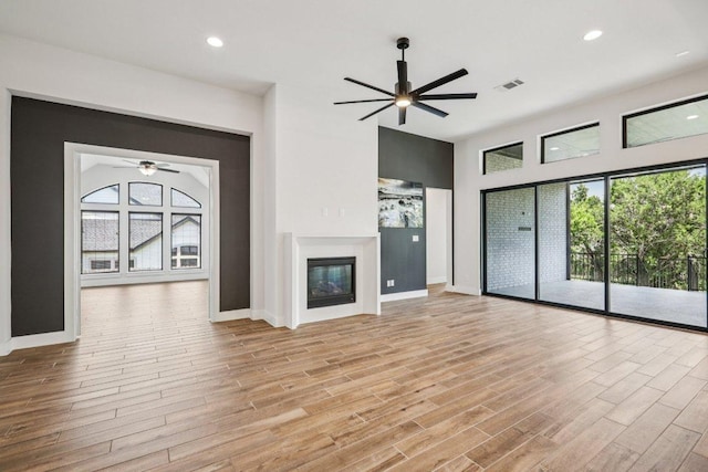 412 Pin Cherry Pass, San Marcos, TX 78666 - unfurnished living room with a ceiling fan, a glass covered fireplace, light wood-type flooring, a high ceiling, and recessed lighting
