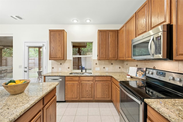 11024 Mint Julep Dr, Austin, TX 78748 - kitchen featuring stainless steel appliances, decorative backsplash, light tile patterned floors, brown cabinets, and light stone countertops
