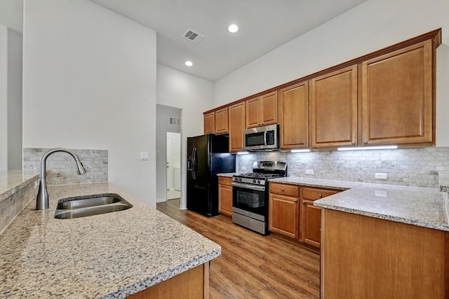 2344 Broken Wagon Dr, Leander, TX 78641 - kitchen with appliances with stainless steel finishes, light stone countertops, tasteful backsplash, light wood finished floors, and brown cabinetry