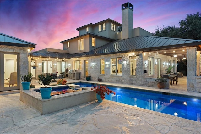 114 Medalist St, Lakeway, TX 78734 - back of property at dusk featuring a standing seam roof, a patio area, outdoor dining space, and stone siding