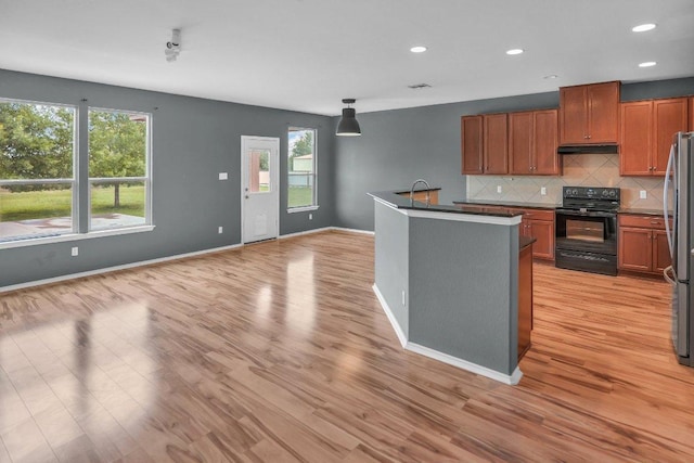 123 Brittany Ln, Bastrop, TX 78602 - kitchen with black range with electric stovetop, under cabinet range hood, light wood-type flooring, tasteful backsplash, and freestanding refrigerator