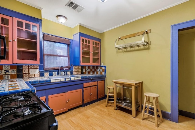 2834 Pearl St, Austin, TX 78705 - kitchen featuring tile counters, tasteful backsplash, light wood-style flooring, crown molding, and black gas stove
