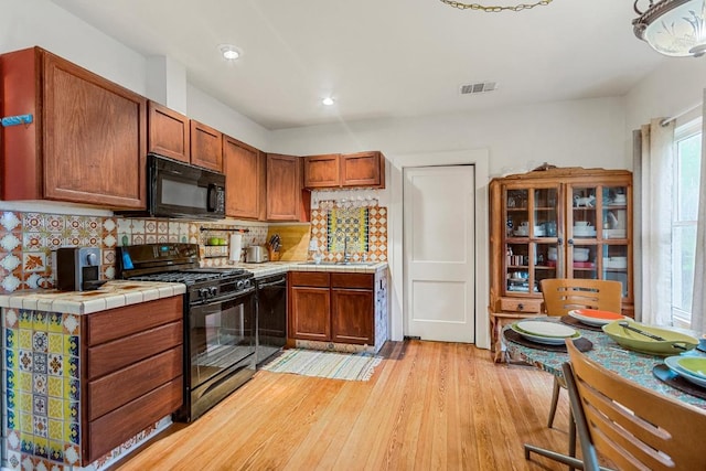 2834 Pearl St, Austin, TX 78705 - kitchen featuring black appliances, tile countertops, light wood finished floors, decorative backsplash, and brown cabinets