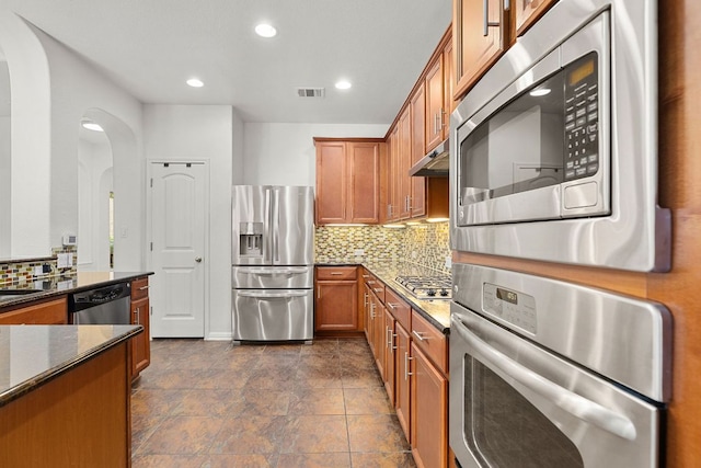 204 Lake Livingston Dr, Georgetown, TX 78628 - kitchen with appliances with stainless steel finishes, arched walkways, brown cabinets, dark stone countertops, and tasteful backsplash