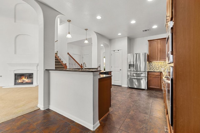 204 Lake Livingston Dr, Georgetown, TX 78628 - kitchen featuring appliances with stainless steel finishes, arched walkways, brown cabinetry, hanging light fixtures, and backsplash
