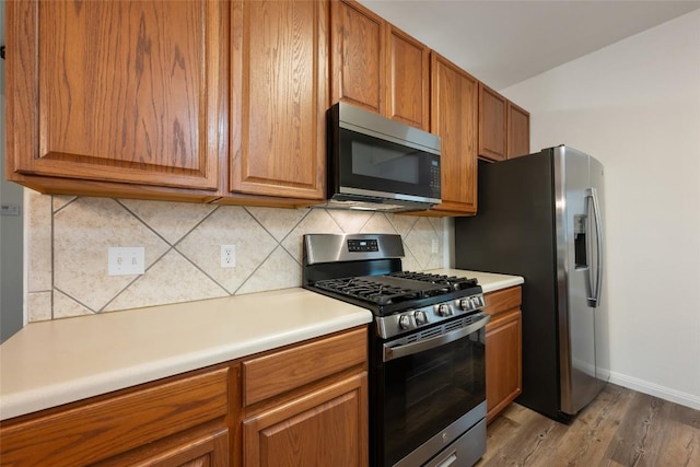 608 Haleys Cv, Leander, TX 78641 - kitchen with appliances with stainless steel finishes, light wood finished floors, brown cabinetry, and decorative backsplash
