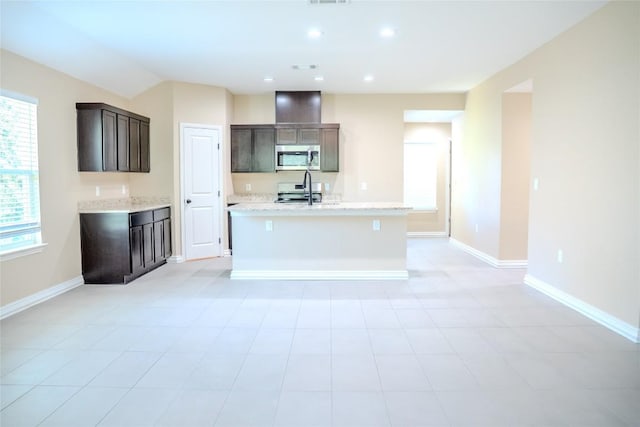 2182 Mcarthur Ave, Kingsland, TX 78639 - kitchen featuring stainless steel microwave, dark brown cabinetry, a center island with sink, range, and light stone countertops