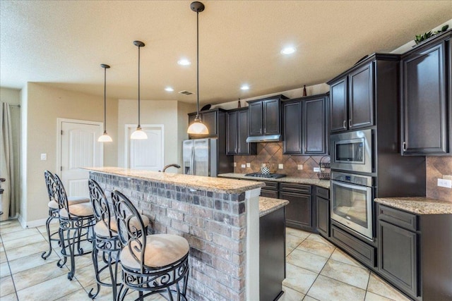 913 Overcup Dr, San Marcos, TX 78666 - kitchen with appliances with stainless steel finishes, backsplash, an island with sink, under cabinet range hood, and a kitchen bar
