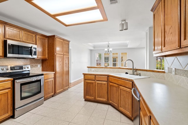 703 Amy Cir, Marble Falls, TX 78654 - kitchen with stainless steel appliances, brown cabinetry, a peninsula, and a raised ceiling
