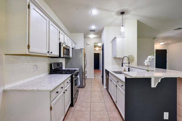 1119 Brinkley Dr, Cedar Park, TX 78613 - kitchen with appliances with stainless steel finishes, a peninsula, tasteful backsplash, a kitchen breakfast bar, and light stone counters