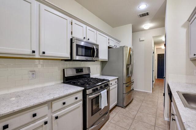 1119 Brinkley Dr, Cedar Park, TX 78613 - kitchen with stainless steel appliances, backsplash, light tile patterned flooring, white cabinets, and light stone countertops