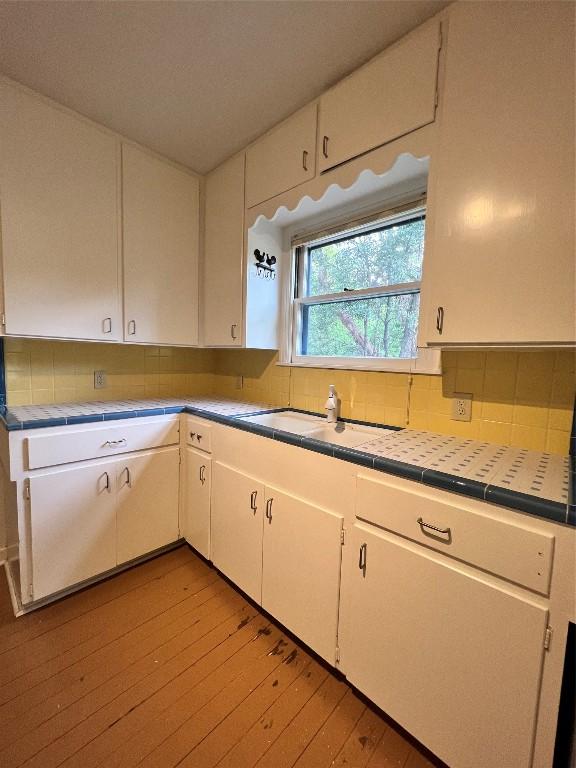 1511 Romeria Dr, Austin, TX 78757 - kitchen with tile counters, light wood-style floors, tasteful backsplash, and white cabinets