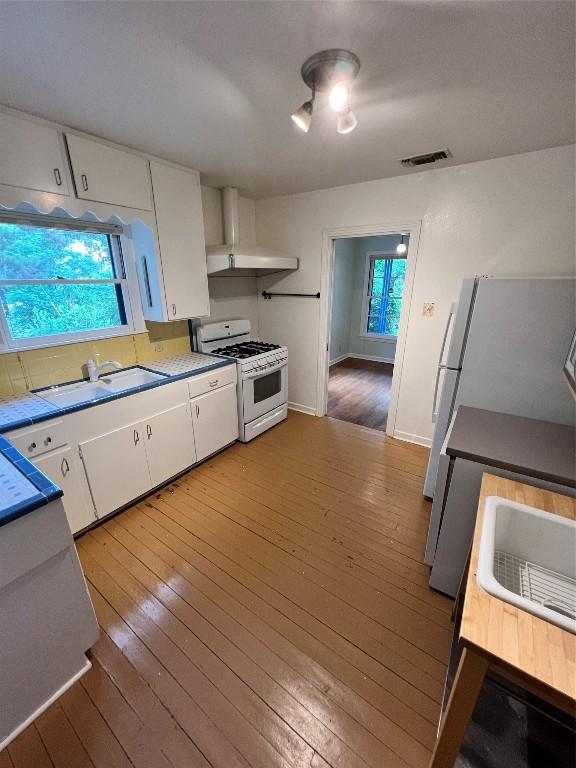 1511 Romeria Dr, Austin, TX 78757 - kitchen featuring white appliances, wall chimney range hood, white cabinetry, light wood-style floors, and healthy amount of natural light