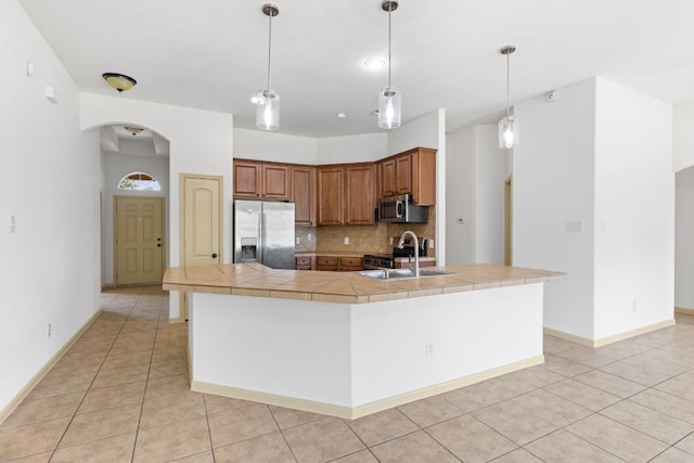 325 Swenson Dr, Hutto, TX 78634 - kitchen featuring stainless steel appliances, arched walkways, light tile patterned floors, tasteful backsplash, and brown cabinets