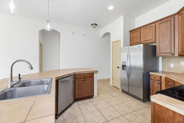 325 Swenson Dr, Hutto, TX 78634 - kitchen featuring stainless steel appliances, arched walkways, brown cabinetry, backsplash, and pendant lighting