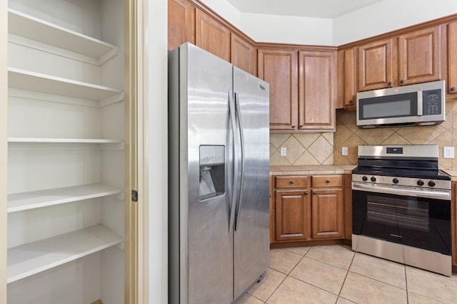 325 Swenson Dr, Hutto, TX 78634 - kitchen featuring appliances with stainless steel finishes, brown cabinetry, light tile patterned flooring, tasteful backsplash, and open shelves