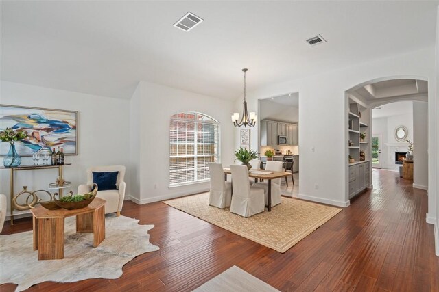4608 Hibiscus Valley Dr, Austin, TX 78739 - dining space with dark wood-style floors, a chandelier, a lit fireplace, and arched walkways