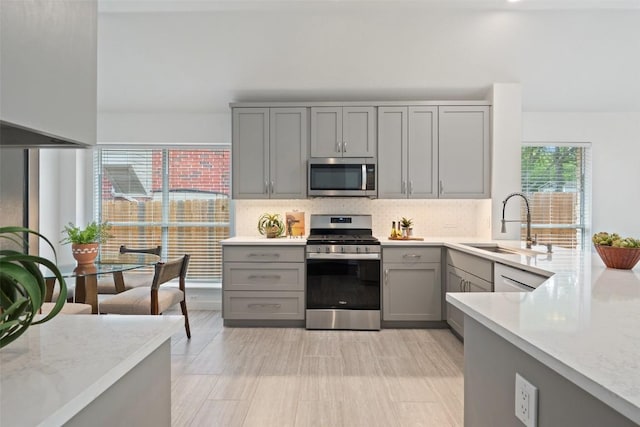 4608 Hibiscus Valley Dr, Austin, TX 78739 - kitchen featuring appliances with stainless steel finishes, gray cabinetry, backsplash, and light stone countertops