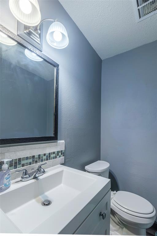 3431 N Hills Dr Unit 115, Austin, TX 78731 - half bathroom with vanity, backsplash, and a textured ceiling