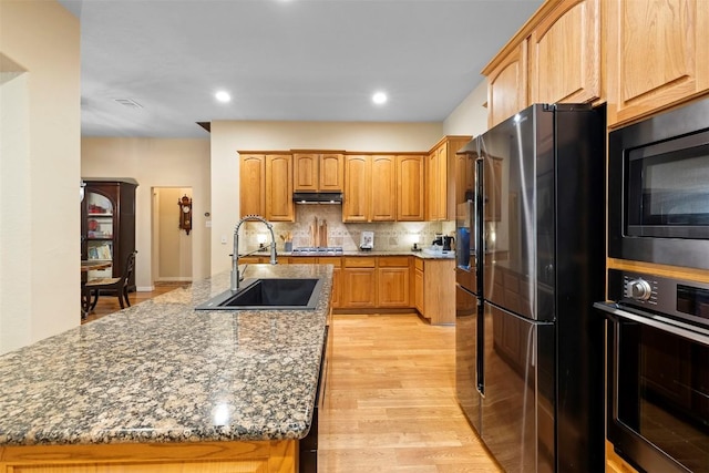 9920 Michelle Hl, Garden Ridge, TX 78266 - kitchen with black appliances, light wood-style floors, dark stone countertops, tasteful backsplash, and a kitchen island with sink