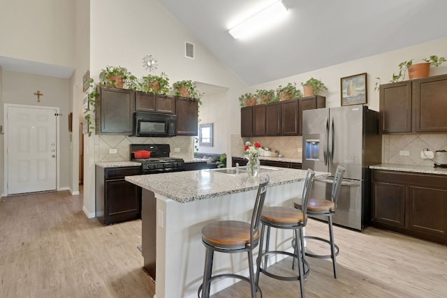 603 Luna Vista Dr, Hutto, TX 78634 - kitchen with black appliances, high vaulted ceiling, dark brown cabinets, light wood finished floors, and tasteful backsplash