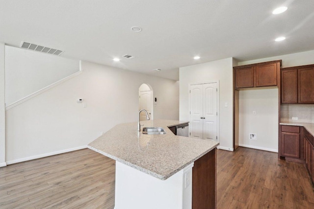 20025 Rhiannon Ln, Pflugerville, TX 78660 - kitchen with wood finished floors, recessed lighting, an island with sink, light stone counters, and arched walkways