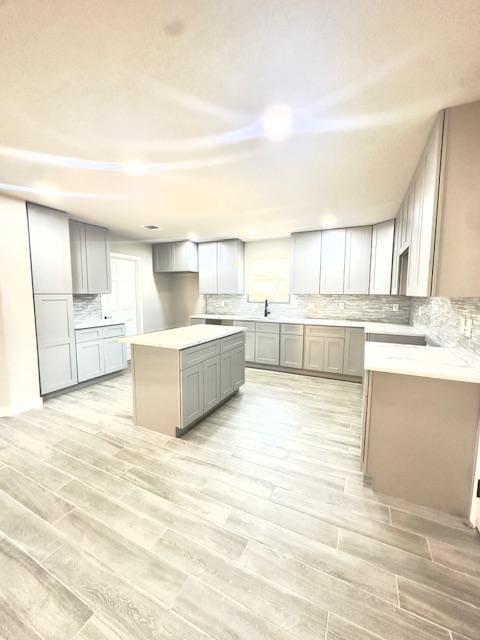 1237 Pelican Pl, New Braunfels, TX 78130 - kitchen with gray cabinets, light wood-style floors, tasteful backsplash, a kitchen island, and light countertops