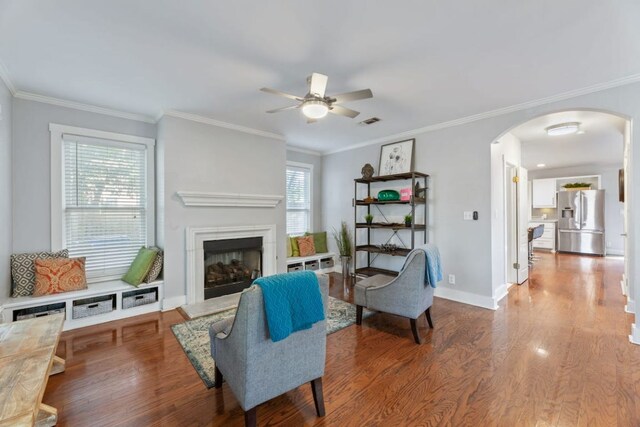 611 W Johanna St, Austin, TX 78704 - living room featuring arched walkways, wood finished floors, a ceiling fan, a fireplace with raised hearth, and ornamental molding